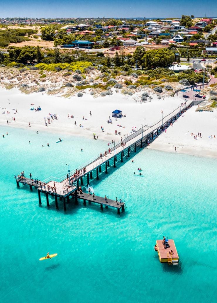 Aerial view over a jetty jutting out over a white sand beach into turquoise water with people swimming and laying on the sand at Coogee Beach, Perth, Western Australia © Tourism Australia
