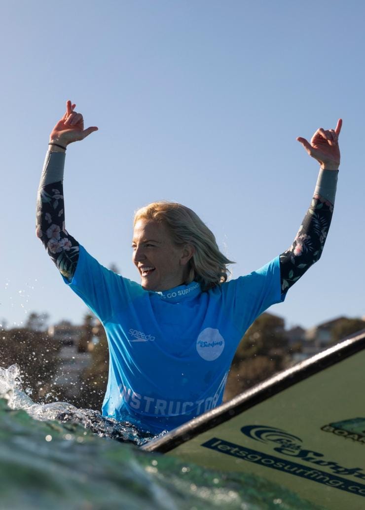 A person riding a board over a wave with their hands in the air during a tour with Let's Go Surfing, Bondi Beach, New South Wales © Destination NSW