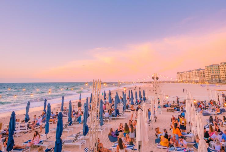 A crowd of people sitting at tables and on beach chairs during sunset on a white sand beach at Moseley Beach Club, Glenelg Beach, Adelaide, South Australia © South Australian Tourism Commission