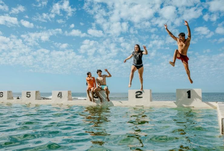 People jumping from diving boards into an ocean bath at Merewether Baths, Newcastle, New South Wales © Destination NSW