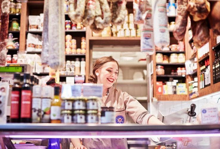 A stallholder smiling behind a counter at the Queen Victoria Market, Melbourne, Victoria © Ewen Bell