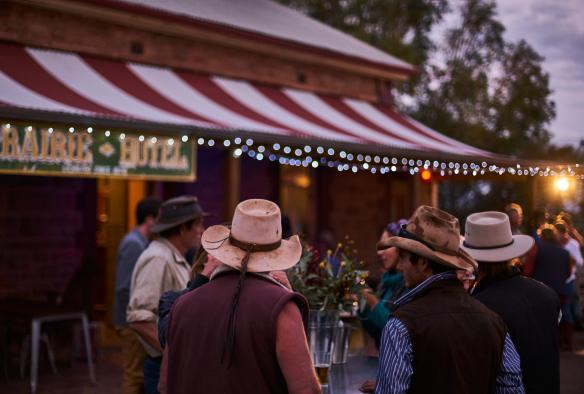 A group of people wearing cowboy hats outside a pub during dusk at Prairie Hotel, Flinders Ranges, South Australia © South Australian Tourism Commission