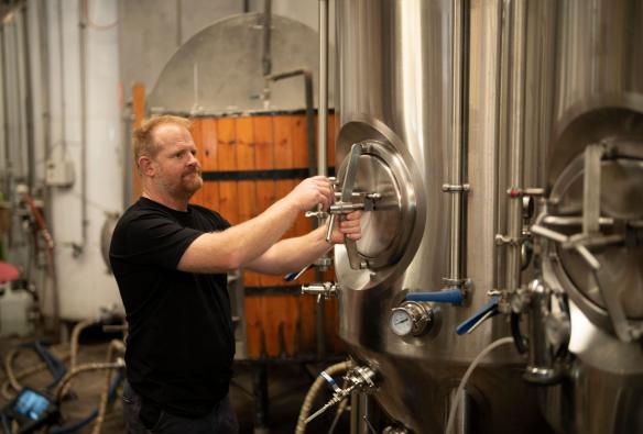 A brewer is seen turning a large stainless steel handle attached to a large brewing vat at the unique working brewery called Black Duck Brewery, Barrington Coast, New South Wales © Tourism Australia