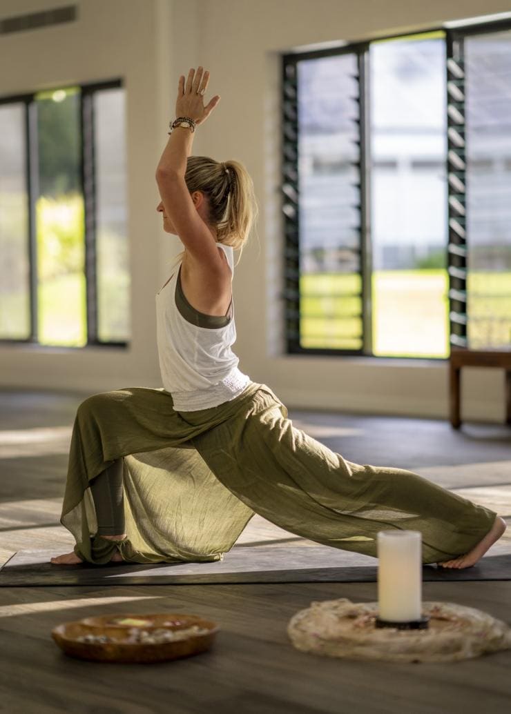 A person standing in a yoga pose in a light-filled room with candles at Eden Health Retreat, Currumbin Valley, Queensland © Tourism and Events Queensland