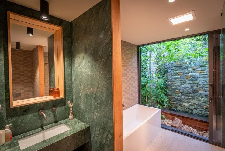 Interior of a bathroom at Samadhi Retreat accommodation, with green marble, a bath and a floor to ceiling window giving way to views of green bushland, Daylesford, Victoria © Samadhi Retreat