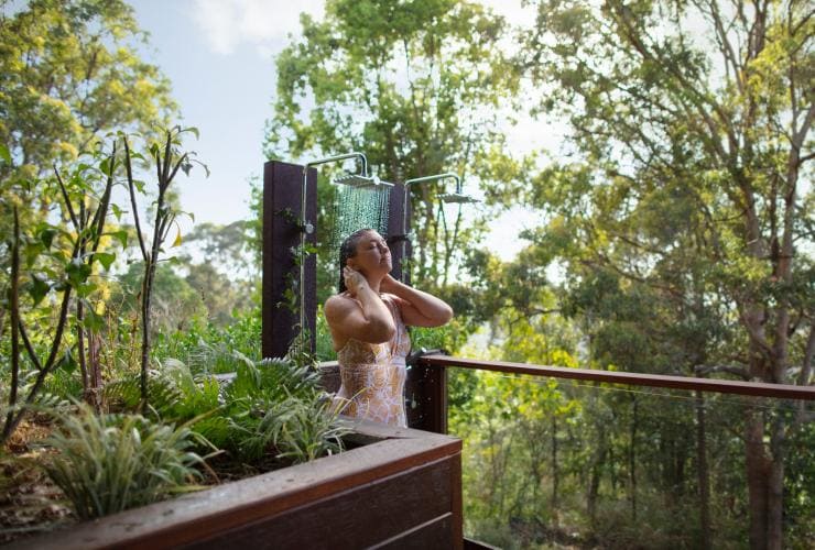 A woman enjoying an outdoor shower amid the trees and plants on a sunny day at Gwinganna Lifestyle Retreat, Gold Coast, Queensland © Destination Gold Coast