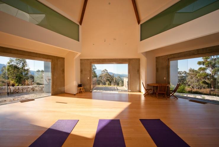 The interior of a light-filled yoga room complete with three purple yoga mats and windows giving way to views of bushland at Harmony Hill Health Retreat, Hobart, Tasmania © Harmony Hill Health Retreat