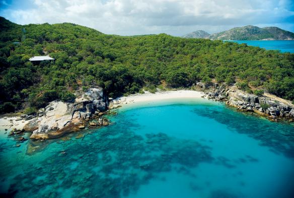 Aerial view over the clear blue ocean towards a white sandy beach, lush trees and accommodation of Lizard Island Resort, Lizard Island, Queensland © Tourism and Events Queensland