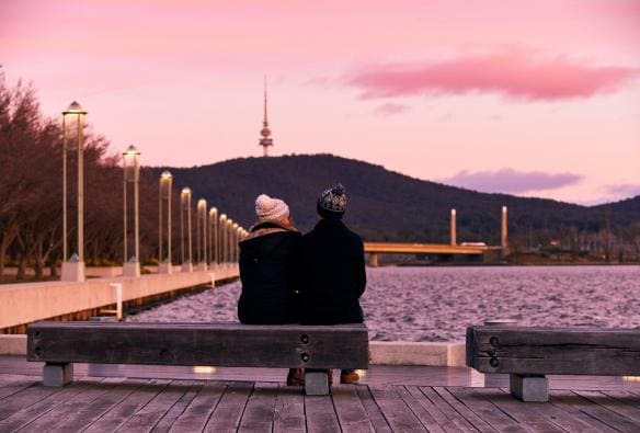 A couple rugged up sitting on a bench beside a lake under a pink sky, Lake Burley Griffin, Canberra, Australian Capital Territory © Lightbulb Studios for Visit Canberra