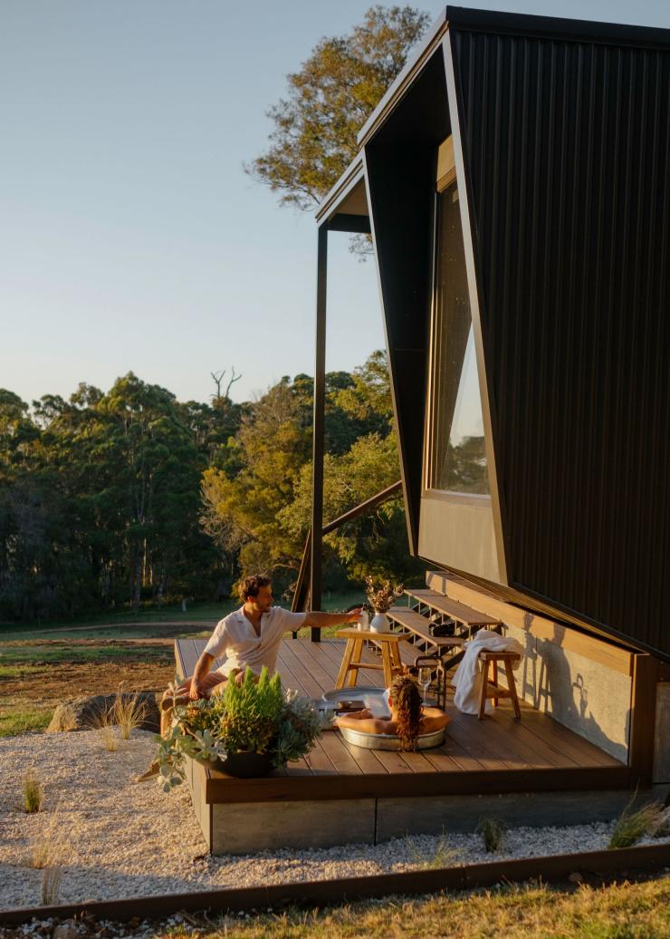 Two people relaxing on the balcony of a tiny home with a tub and lush trees, Heyscape Denmark, Australia's Southwest, Western Australia © Rachel Claire / Heyscape Denmark