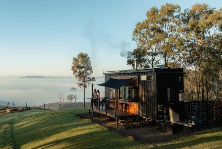 A couple standing on the balcony of a tiny house perched on top of a green hill, Baya Tiny House, Scenic Rim, Queensland © Tourism and Events Queensland