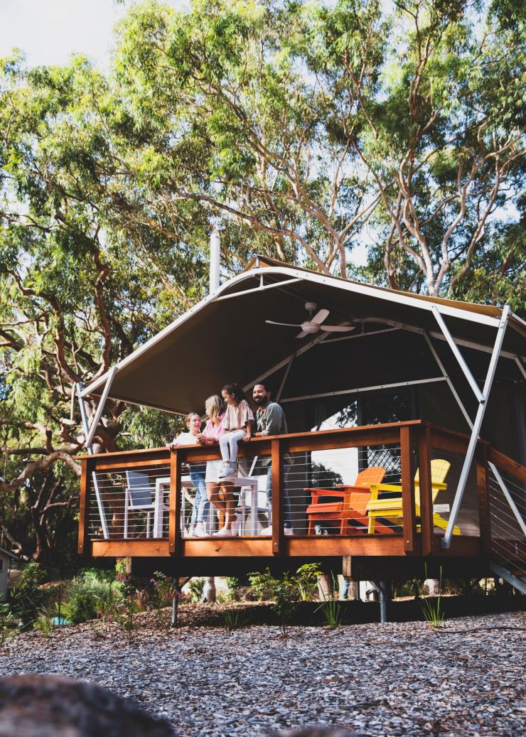 A family standing on a cabin balcony overlooking bushland, Port Stephens Koala Sanctuary, Port Stephens, New South Wales © Destination NSW 