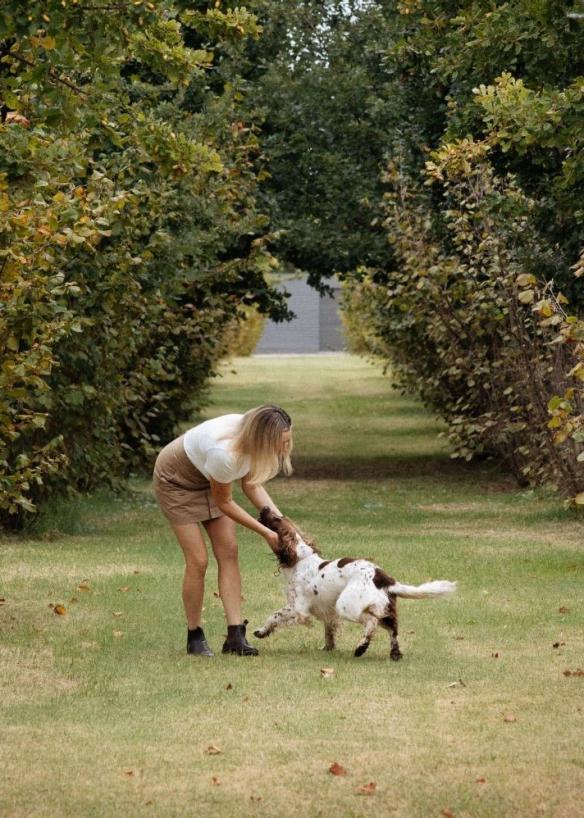 An owner at Beltana Farm shares a warm moment with a truffle dog on a grassy path between a long row of tall, evenly spaced trees, Canberra, Australian Capital Territory © Tourism Australia