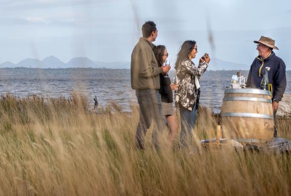 Visitors tasting oysters around a wine barrel with mountains in the background at Devil's Corner Winery, East Coast, Tasmania © Stu Gibson