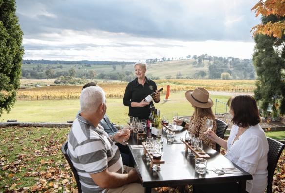 A group of guests sit around an outdoor table, overlooking a winery at Wines, Riverina, New South Wales © Tourism Australia