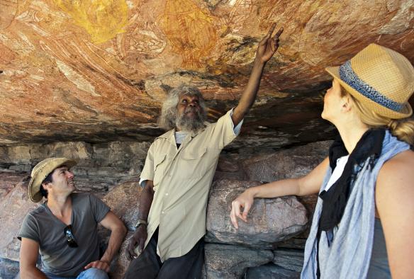 An Aboriginal guide describing ancient rock art to guests standing beneath a rocky outcrop with Lords Kakadu & Arnhem Land Safaris, Injalak Hill, Northern Territory © Shaana McNaught 