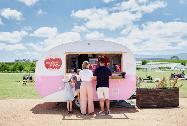 A family standing beside a pink food truck with picnic tables on a field behind it at Cherry Hill Orchard, Yarra Valley, Victoria © Tourism Australia 