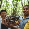 An Indigenous guide holding up a mud crab as a tour participant smiles widely behind him, Walkabout Cultural Adventures, Daintree Rainforest, Queensland © Tourism and Events Queensland