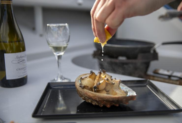 A person squeezing lemon on fresh abalone with a glass of white wine, Seafood Seduction, Hobart, Tasmania © Daniel Tran