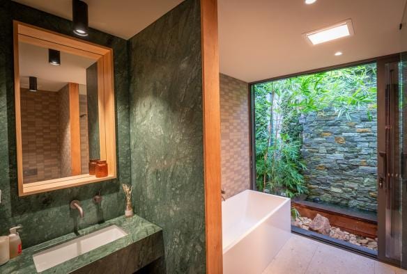 Interior of a bathroom at Samadhi Retreat accommodation, with green marble, a bath and a floor to ceiling window giving way to views of green bushland, Daylesford, Victoria © Samadhi Retreat