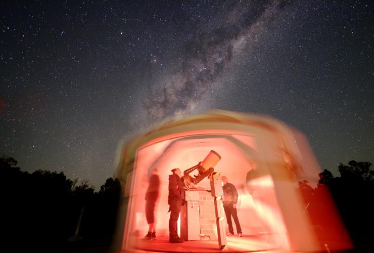 Three people standing around a telescope in a dome lit up with red lights with the starry sky above them at Perth Observatory, Bickley, Western Australia © Perth Observatory/Andrew Lockwood