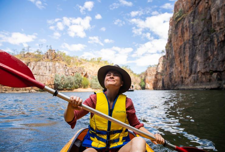 A person smiling while canoeing through a calm gorge surrounded by towering orange cliffs, Nitmiluk Tours, Nitmiluk National Park, Northern Territory © Tourism Northern Territory/Helen Orr 