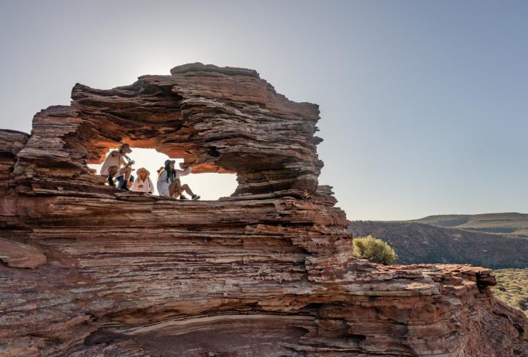 A group of hikers sitting inside a jagged hole inside a red rock formation in Kalbarri National Park, Western Australia © Tourism Australia