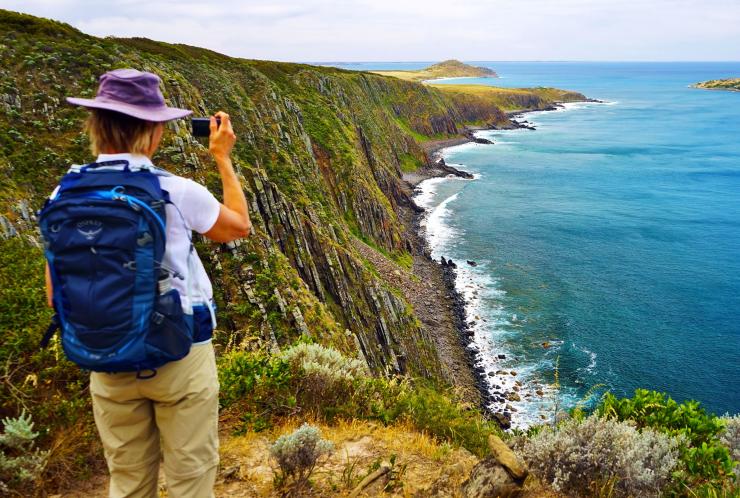 A hiker pausing to take a photo as they gaze out at a rugged coastline and blue ocean on the Southern Ocean Walk in South Australia © Southern Ocean Walk