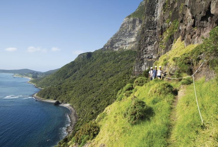 A group of people hiking in helmets with a rope alongside a mountain by the coast, Mount Gower, Lord Howe Island, New South Wales © Destination NSW