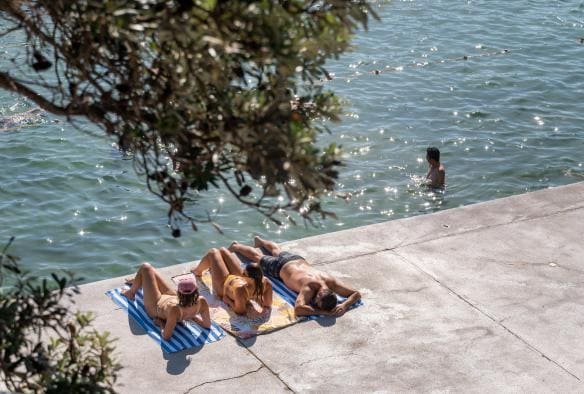 Three friends laying on towels at the water's edge at The Entrance, Central Coast, New South Wales © Tourism Australia