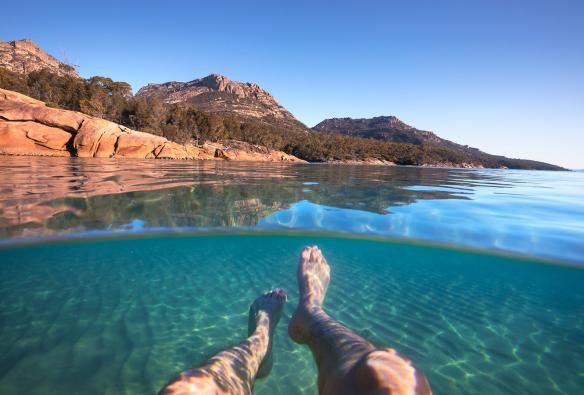 Man swimming with mountains in the background at Honeymoon Bay, Freycinet, Tasmania © Tourism Australia