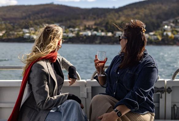 Two women sitting beside the side of a boat looking out to the ocean. One has a glass of wine in hand, Tasmanian Wild Seafood Adventures, Hobart, Tasmania © Dearna Bond
