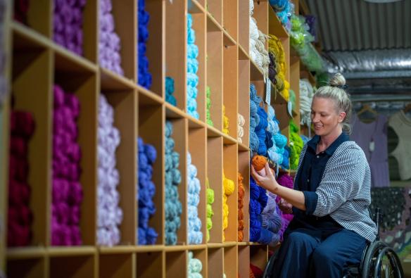 Woman using a wheelchair admires bright yarn at Nundle Woolen Mill, New England, New South Wales © Tourism Australia