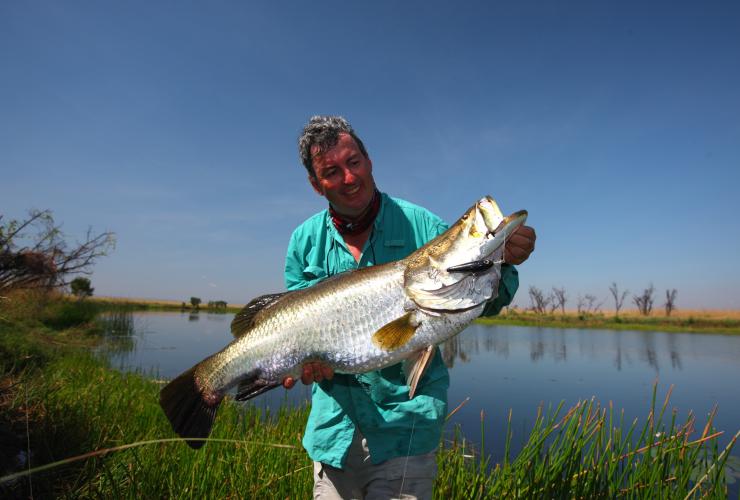 A man holding a large fish beside a calm waterhole, HeliSpirit, Kimberly, Western Australia © HeliSpirit
