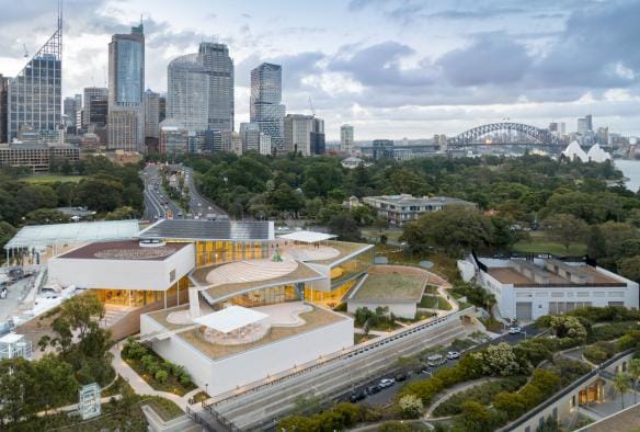 Aerial view over a tiered building with outdoor sculptures surrounded by green trees with a city skyline behind it at the Art Gallery of New South Wales, Sydney, New South Wales © Art Gallery of New South Wales / Tourism Australia