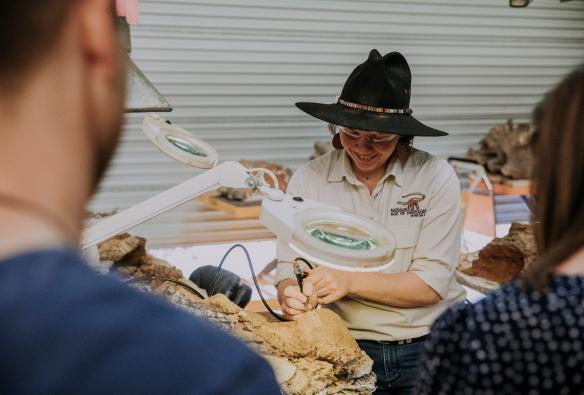 A museum worker carefully uncovering fossils under a magnifying glass at the Australian Age of Dinosaurs museum, Winton, Queensland © Tourism and Events Queensland