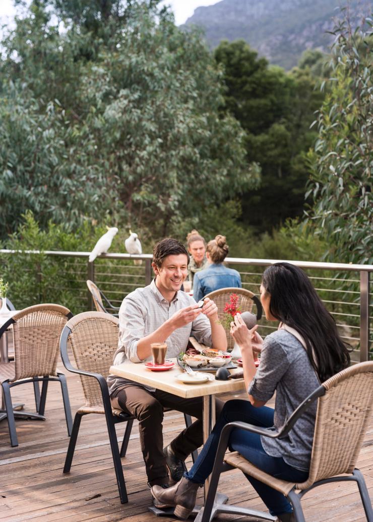 Groups of people enjoying coffee on an outdoor terrace with cockatoos on a railing overlooking trees,  Brambuck National Park and Cultural Centre, Grampians, Victoria © Rob Blackburn
