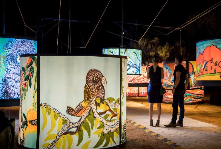 Two people standing among a kaleidoscope of colourful art installations adorned with pictures of native birds at Parrtjima - A Festival in Light, Alice Springs, Northern Territor © Tourism NT/James Horan