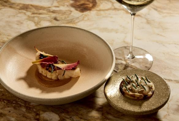 A marble table with two carefully plated dishes and a glass of white wine at LVN, Bird in Hand, Adelaide Hills, South Australia © Bird in Hand