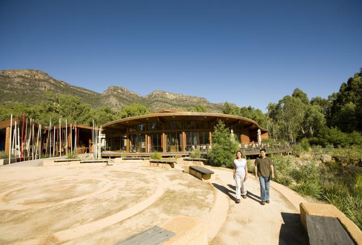 Two people walking near an Aboriginal cultural centre nestled amid bushland and rocky peaks, Brambuk Aboriginal Cultural Centre, The Grampians, Victoria © Visit Victoria