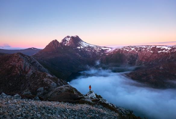 A person standing on a rocky peak overlooking low hanging clouds over an alpine landscape, Hansons Peak, Cradle Mountain, Tasmania © Daniel Tran