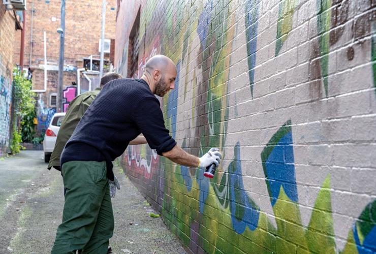 Two people learning to spray paint street art in a laneway, Localing Tours, Melbourne, Victoria © Tourism Australia