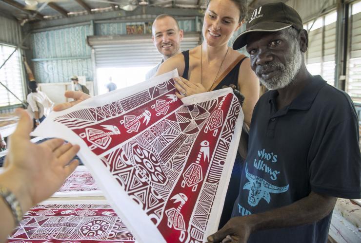 Deux personnes souriant avec un artiste aborigène tout en tenant une œuvre d'art, Tiwi by Design, Tiwi Islands, Territoire du Nord © Shaana McNaught