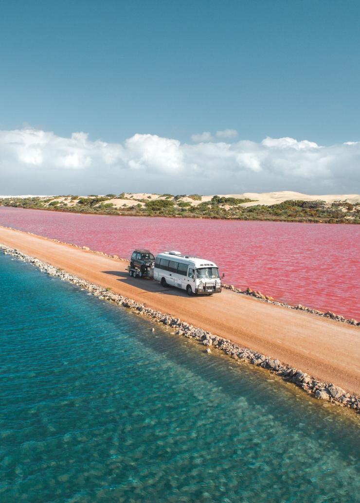 Vue aérienne d'une voiture roulant le long d'un chemin de terre entre un lac bleu et un lac rose à Lake MacDonnell, Eyre Peninsula, Australie du Sud © Jaxon Foale