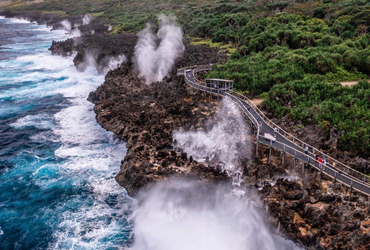 Personnes sur un sentier entre une série de geysers spectaculaires en pleine éruption dans l'océan, et bush vert luxuriant aux Blowholes, Christmas Island © Christmas Island Tourism Association
