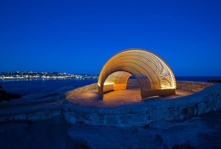 Une sculpture en forme de coquillage illuminée de lumières dorées à la tombée du soir, Dynamics in Impermanence par Nicole Larkin, Sculpture by the Sea, Bondi, Nouvelle-Galles du Sud © Rein Photography