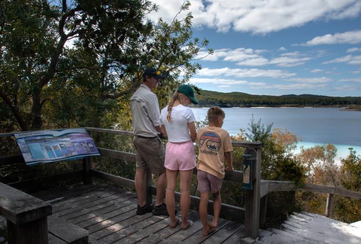 Enfants debout aux côtés d'un guide touristique sur un belvédère surplombant un lac près du Kingfisher Bay Resort, K'gari, Queensland © Tourism and Events Queensland