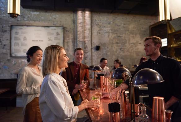 Un groupe souriant se tenant devant le comptoir d'un bar, des boissons à la main, à Archie Rose Distillery, Sydney, Nouvelle-Galles du Sud © Destination NSW