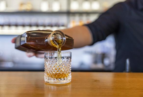 Gros plan d'une main tenant une bouteille, versant un spiritueux foncé dans un verre à whisky à la Bass & Flinders Distillery, Mornington Peninsula, Victoria © Tourism Australia
