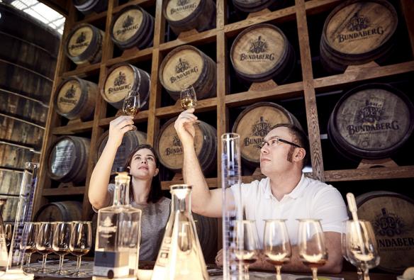 Un homme et une femme tenant des verres remplis de rhum en l'air, les observant à la lumière, lors de la création de leur propre rhum (Blend Your Own Rum Experience) à la Bundaberg Rum Distillery, Bundaberg, Queensland © Bundaberg Rum